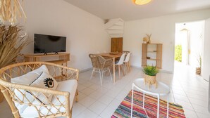 A modern living room with a TV, wicker furniture, a dining table, and a colorful rug.