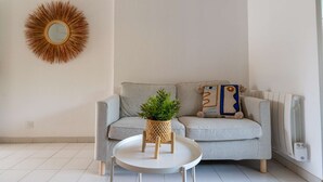 A living room with a grey sofa, a round coffee table, a potted plant, a decorative mirror, and a radiator.
