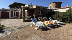 Un bâtiment en pierre avec un toit en tuiles, un petit patio doté de chaises longues et une zone recouverte de gravier.
