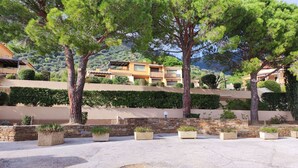 A courtyard with potted plants, a stone wall, and a building with a sloped roof in the background. - T2 en rez de jardin , proche plage de St Clair et commerces (LE LAVANDOU)
