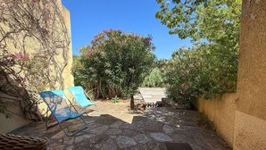 A stone-paved courtyard with a blue chair, a wicker basket, and a tree with pink flowers. - T2 en rez de jardin , proche plage de St Clair et commerces (LE LAVANDOU)