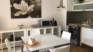 A modern kitchen with white cabinetry, a microwave, an oven, and a dining area with a table and chairs. - T2 en rez de jardin , proche plage de St Clair et commerces (LE LAVANDOU)