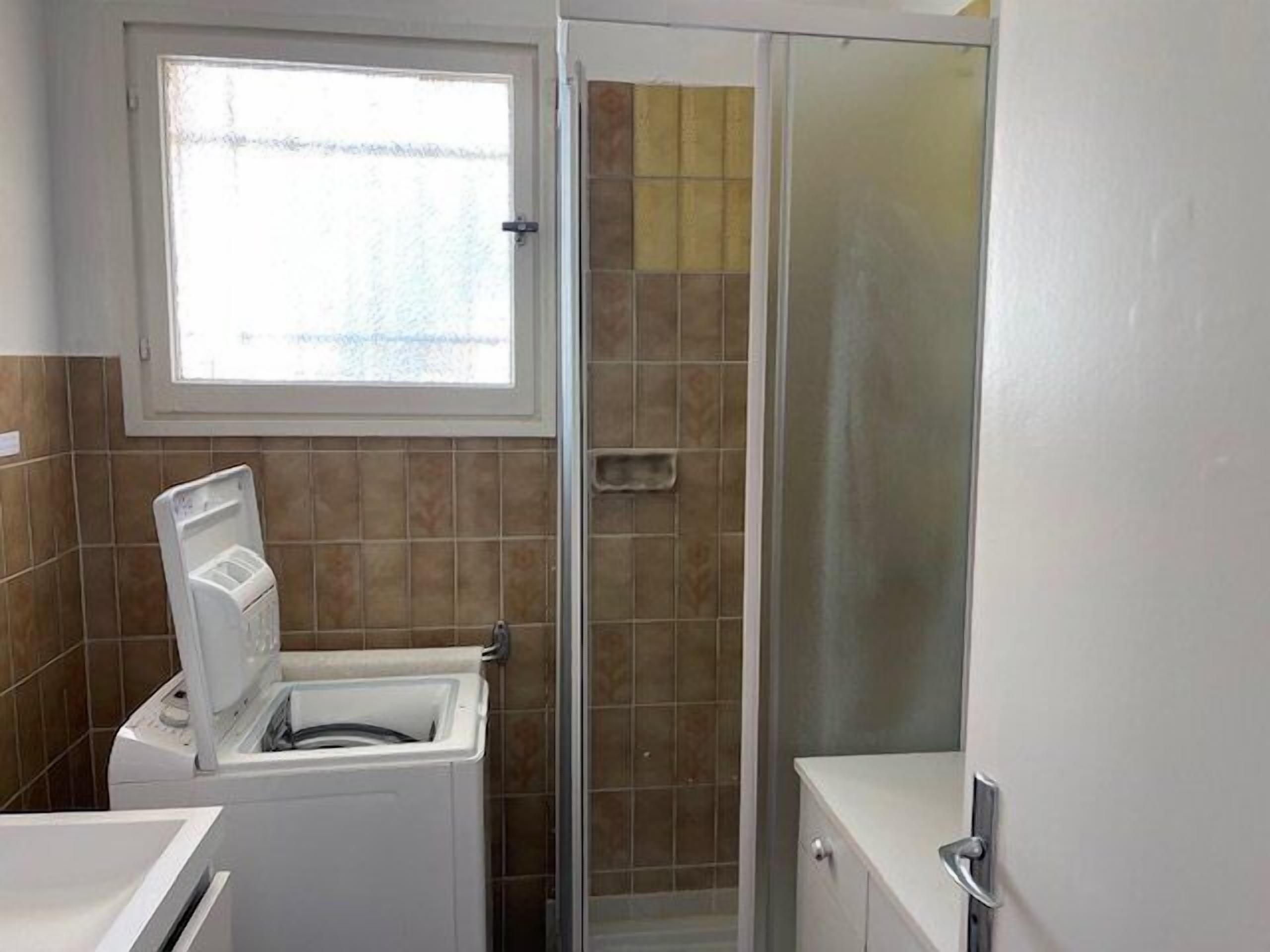 A bathroom with a washing machine, a glass shower enclosure, and a window.
