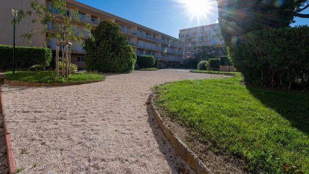 Une cour avec un chemin de gravier, des pelouses verdoyantes et un immeuble à plusieurs étages doté de balcons.