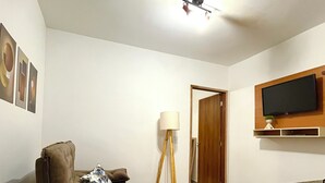 Ett modernt vardagsrum med en soffa, ett soffbord, en golvlampa och en tv som är monterad på väggen.
