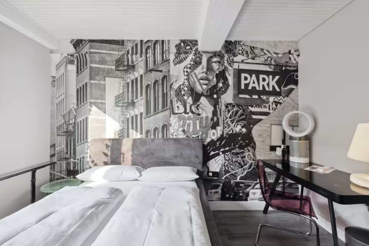 Ein modernes Hotelzimmer mit einem großen Bett, einem Schreibtisch mit Stuhl, einem kleinen Tisch und einer Wandmalerei.