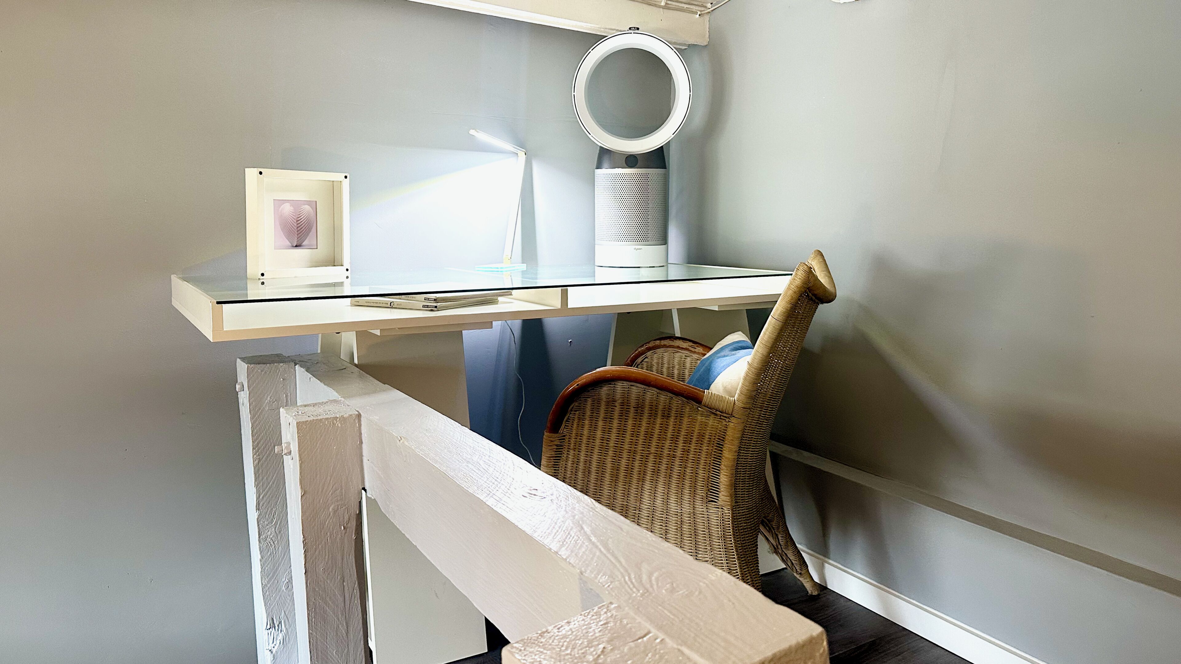 Una habitación con un escritorio, una silla, un cuadro enmarcado y una luz de aro.