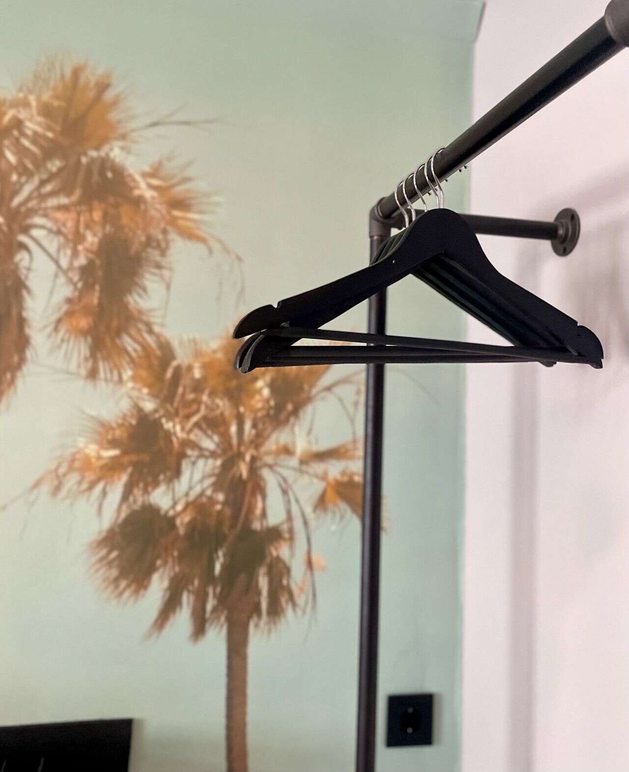 A black coat hanger against a wall with a palm tree painting.