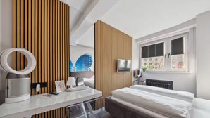 A modern bedroom with a bed, bedside table, mirror, and a window with blinds. - The Room 44 (Hamburg)