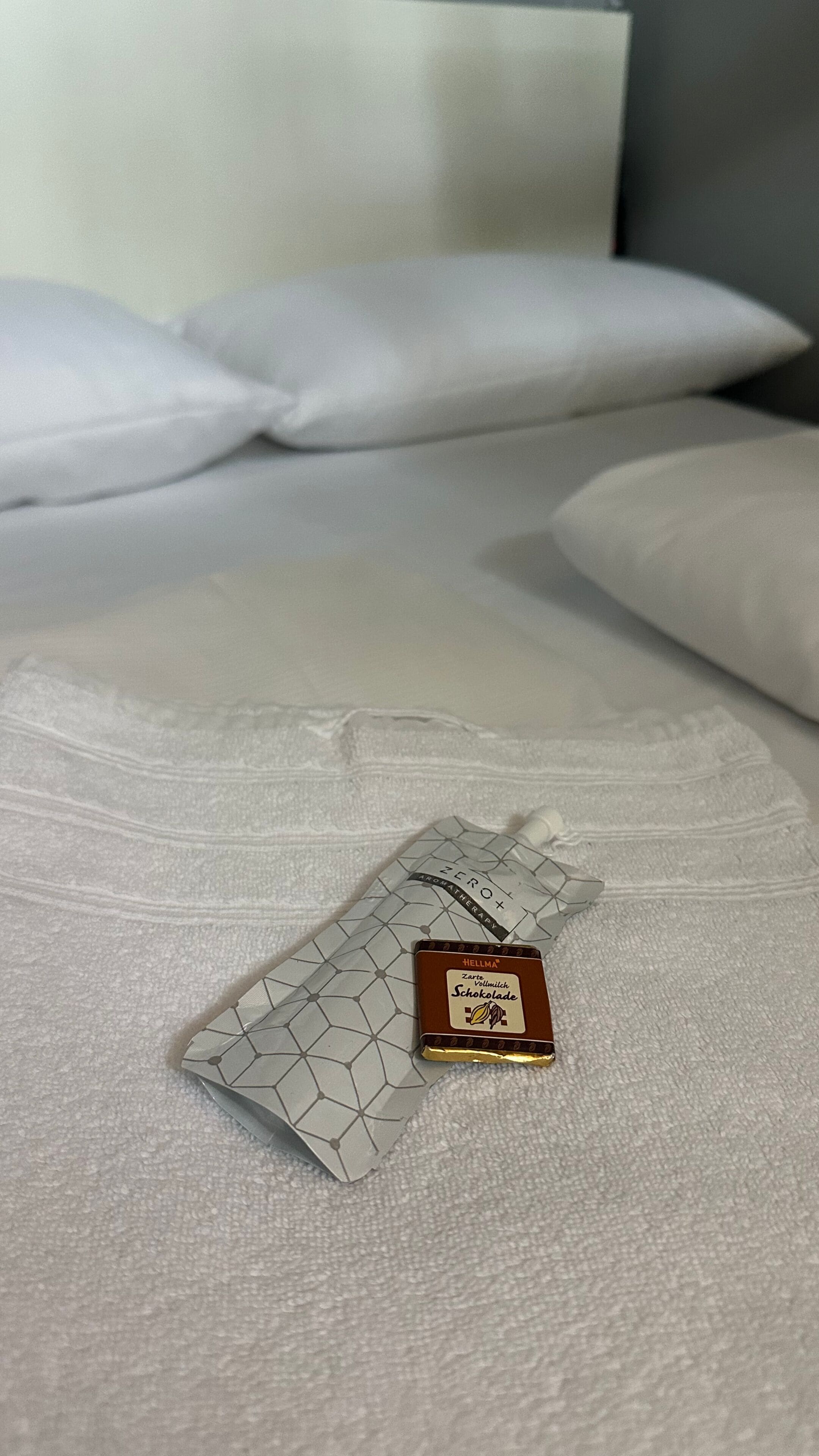 A bed with white linens and a small chocolate bar on the bedspread.