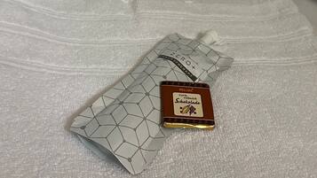 A bed with white linens and a small chocolate bar on the bedspread.