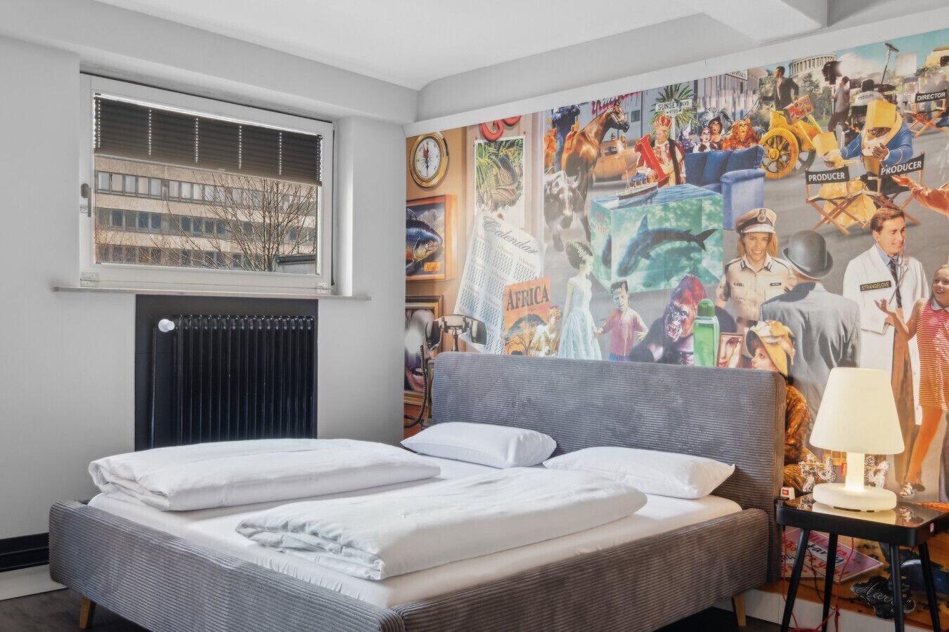 Habitación de hotel con cama, radiador, ventana con persianas y un gran mural en la pared.