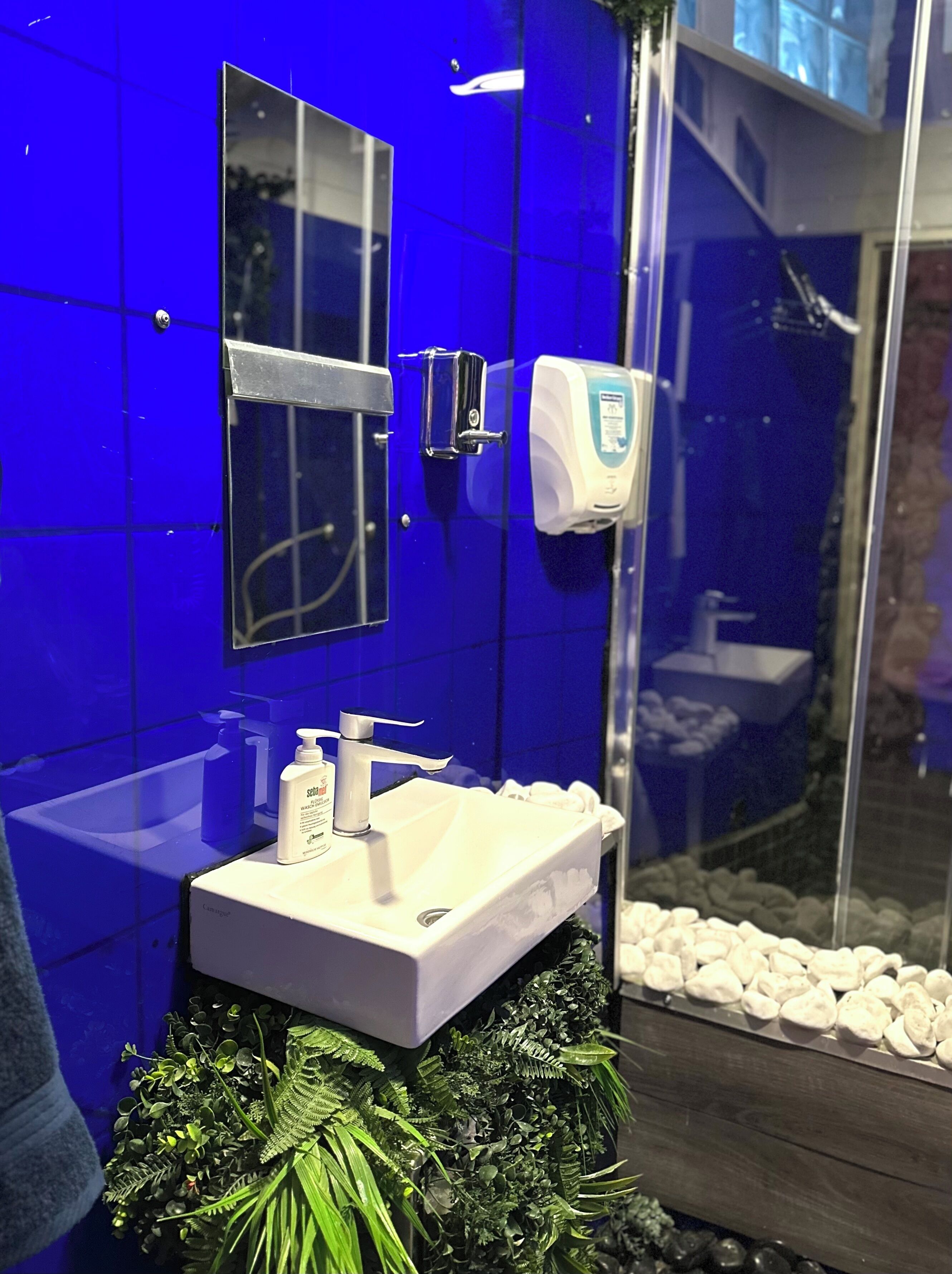 Une salle de bain avec un lavabo blanc, un miroir et un distributeur de gel hydroalcoolique.