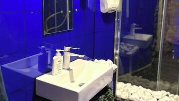 Une salle de bain avec un lavabo blanc, un miroir et un distributeur de gel hydroalcoolique.