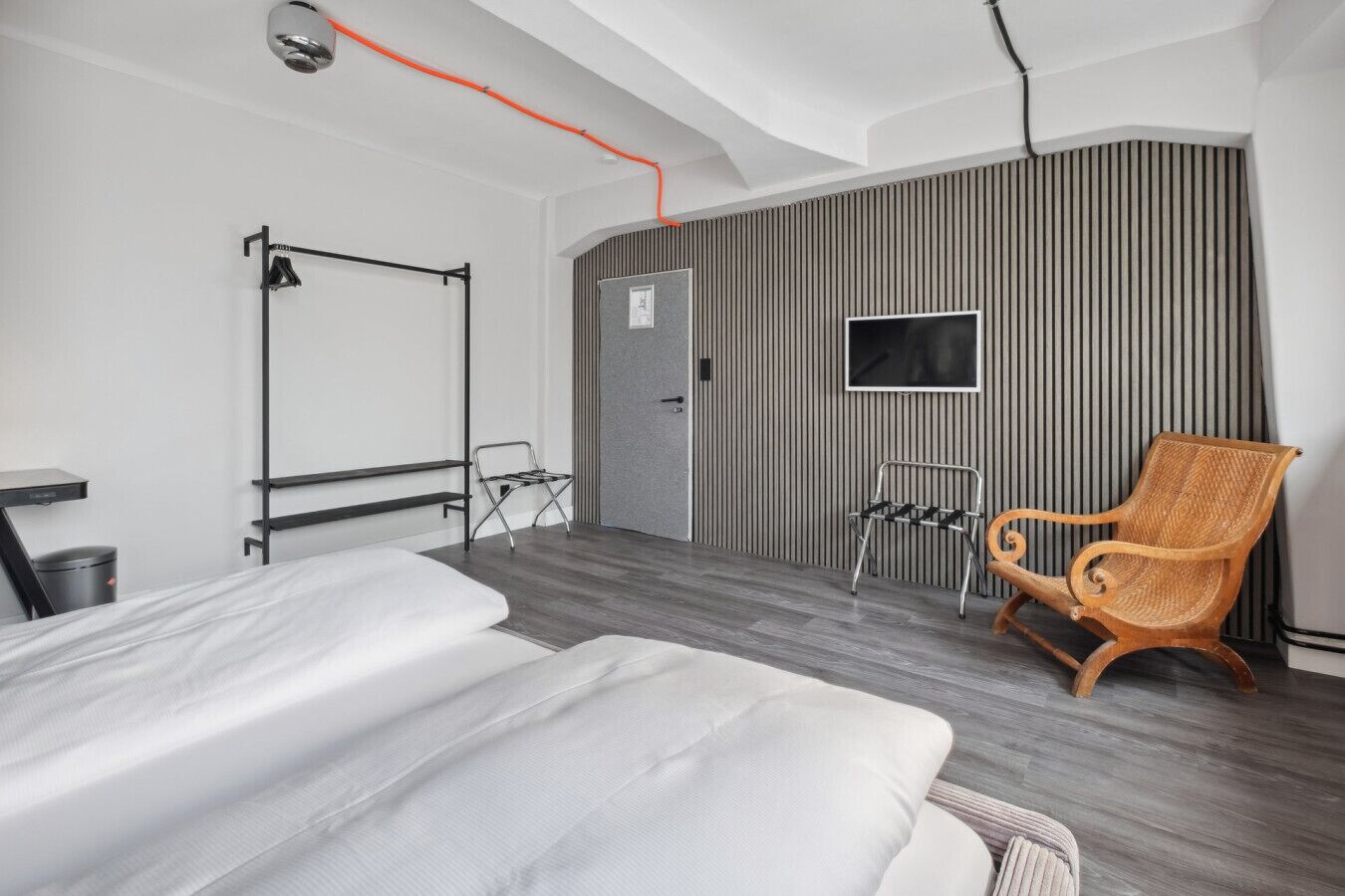 A modern hotel room with a bed, a wooden chair, a TV, and a striped wall.