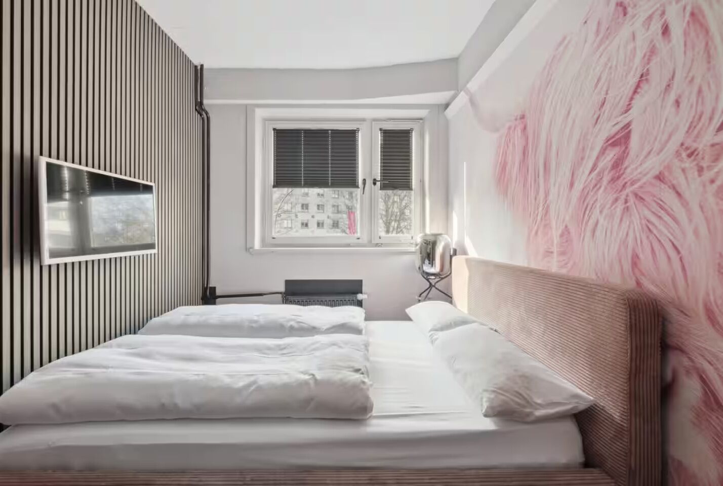Quarto moderno com cama grande, televisão de tela plana na parede e janela com persianas.