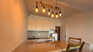 A modern kitchen with white cabinets, a wooden dining table, and a unique light fixture.