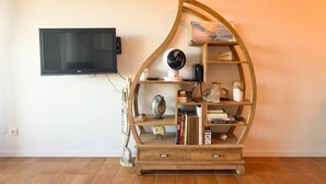A living room with a curved wooden bookshelf, a flat-screen TV mounted on the wall, and a tiled floor.