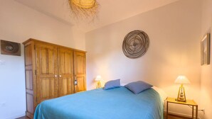 A bedroom with a bed, two bedside tables with lamps, a wooden wardrobe, and a wall art piece.