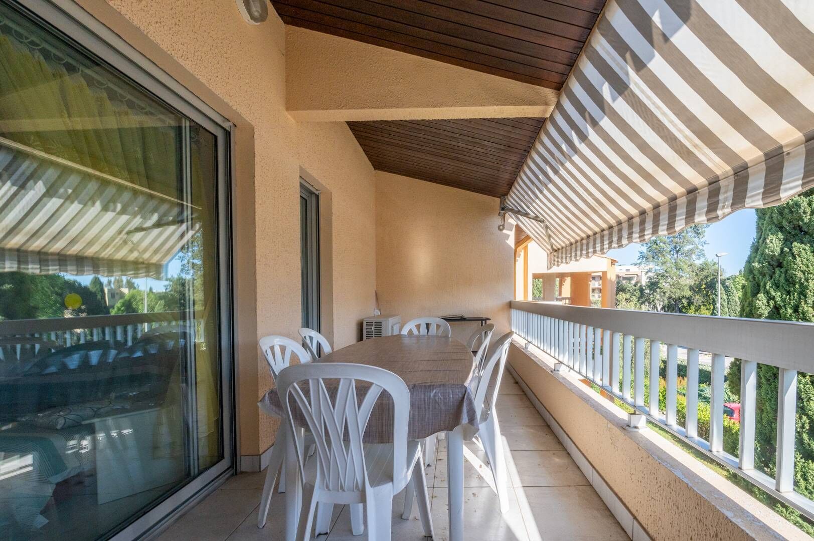 Ein überdachter Balkon mit Tisch und Stühlen, eine Glastür und Blick ins Grüne.