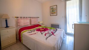 Un dormitorio con cama, mesita de noche, lámpara, silla, radiador y ventana con cortinas.