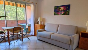 Un salon avec un canapé, une table entourée de chaises, une lampe et un tableau accroché au mur.