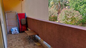 Un balcon avec une table en bois, une chaise rouge et un étendoir en métal.