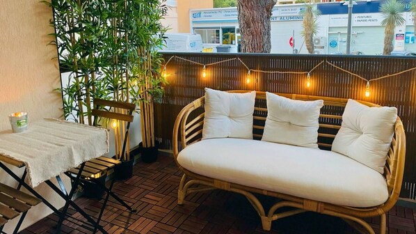 An outdoor seating area with a wicker sofa and a table, surrounded by bamboo plants and string lights.