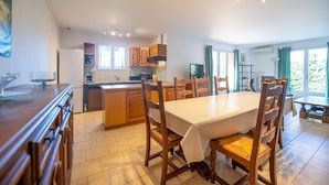 A modern kitchen with wooden cabinets, a dining table, and chairs. - Maison, climatisée plage St Clair et commerces (LE LAVANDOU)