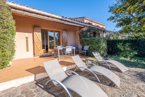 A building with a tiled roof, a patio with lounge chairs, and a wooden door. - Maison, climatisée plage St Clair et commerces (LE LAVANDOU)