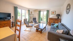 A living room with a television, sofa, chairs, a table, and a cabinet. - Maison, climatisée plage St Clair et commerces (LE LAVANDOU)