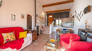 Ein geräumiger Wohnbereich mit einem roten Sofa, einem roten Sessel und einem Glastisch. Im Hintergrund ist eine Küche mit Esstisch und Stühlen zu sehen.