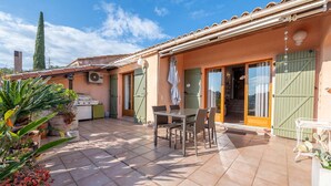 Eine Terrasse mit Tisch und Stühlen, einer kleinen Küchenzeile und einer Tür zu einem Zimmer.