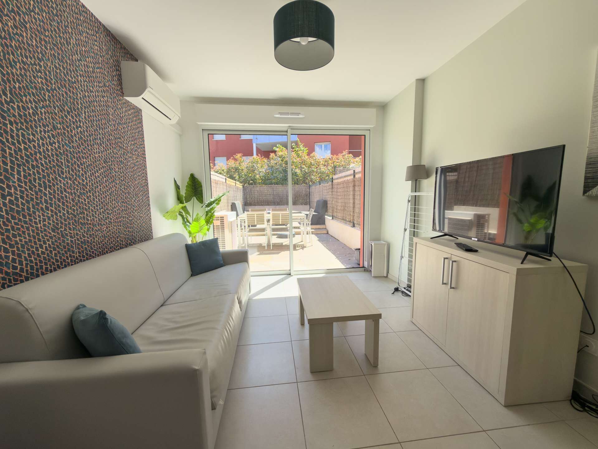 A modern living room with a sofa, a coffee table, a TV, and a sliding glass door leading to an outdoor patio.