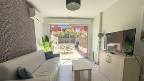 Un salon moderne comprenant un canapé, une table basse, un téléviseur et une porte-fenêtre coulissante donnant sur une terrasse extérieure.