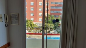 Ein Hotelzimmer mit Blick auf einen Swimmingpool, Sitzgelegenheiten im Freien und ein rotes Gebäude im Hintergrund.