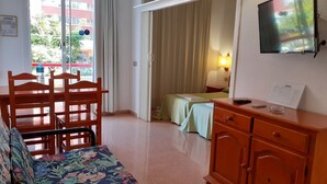 Ein Hotelzimmer mit Bett, Schreibtisch, Stuhl, Sofa, Fernseher und einem Fenster mit Vorhängen.