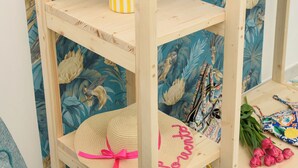 Une étagère en bois, avec un papier peint à motifs floraux en arrière-plan, un vase à rayures, un chapeau de paille et quelques sacs.