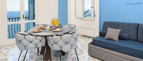 A dining area with a table set for two, a sofa, and a view of the sea.