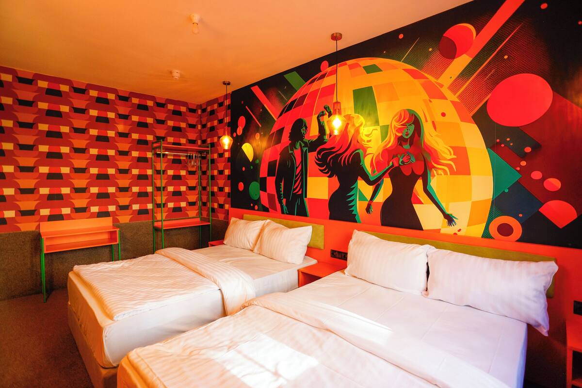 A hotel room with two beds, a checkered wall pattern, and a colorful mural on the wall.