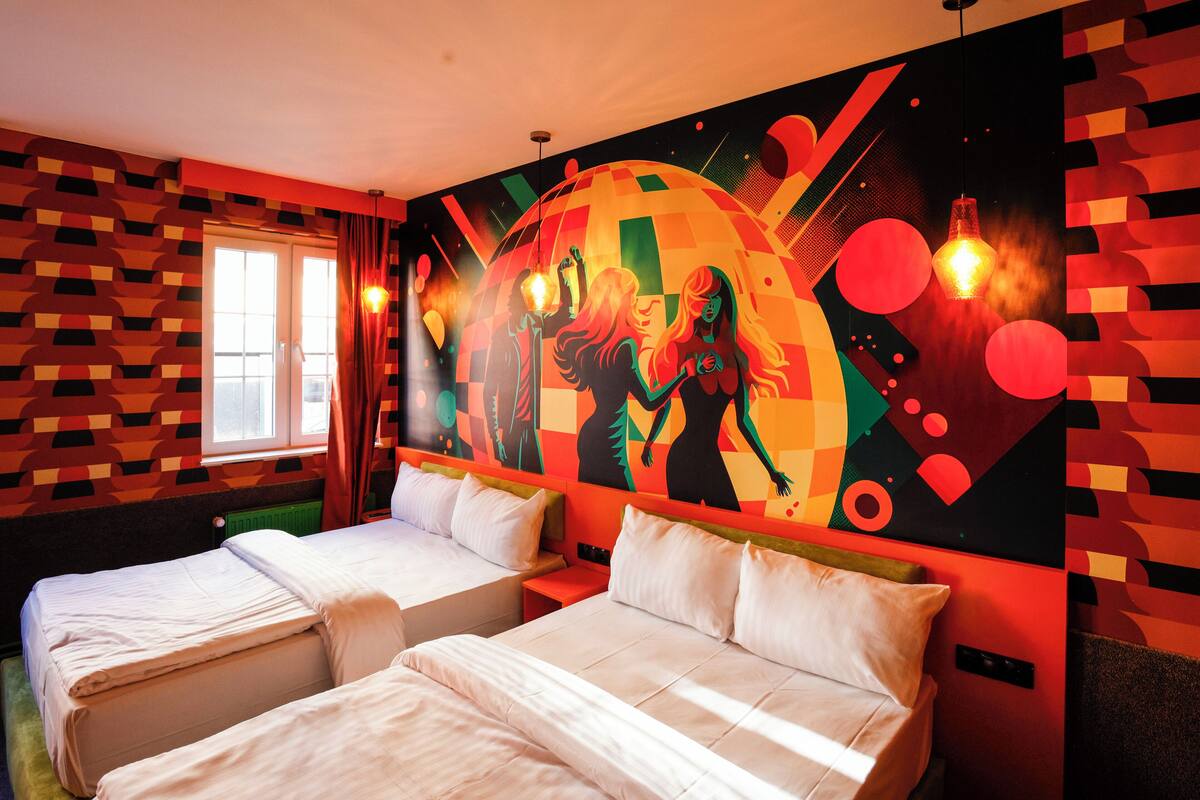 A hotel room with two beds, a large abstract mural on the wall, and a window with curtains.