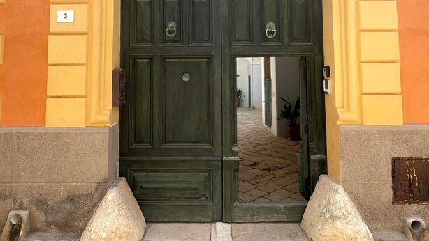 A double door with a dark green finish, flanked by two stone bollards, leading into a building with yellow and beige walls. - BUILDING COSI-FORINA (Morciano di Leuca)