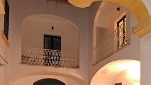 A courtyard with a tiled floor, potted plants, a wooden door, and a balcony with a metal railing. - BUILDING COSI-FORINA (Morciano di Leuca)