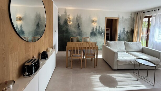 A modern living room with a dining area, a large mirror, and a forest-themed wall mural. - Superb 6-person T3 apartment close to the slopes (Péone)