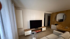 A modern living room with a flat-screen TV, a sofa, a small side table, and a wooden accent wall with a mirror. - Superb 6-person T3 apartment close to the slopes (Péone)