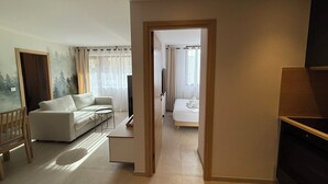 A modern living room with a sofa, a small table, and a TV. There is a doorway leading to another room with a bed. - Superb 6-person T3 apartment close to the slopes (Péone)