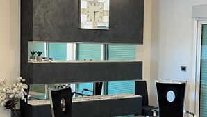 Un interior moderno con una pared de acento negra, un respaldas de espejo y un comedor con mesa de vidrio y dos sillas.