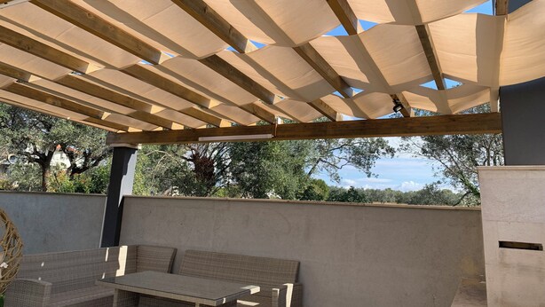 Een terras buiten met een houten pergola, een tafel en stoelen.