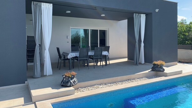 Un patio exterior moderno con piscina, que incluye un comedor con sillas y una mesa, y dos macetas decorativas.