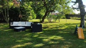 Un área de estar al aire libre con un sofá y dos otomanas cuadradas, rodeada de césped y árboles.